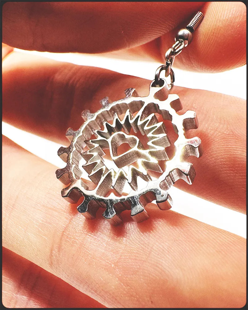 Image of hand holding a shiny stainless steel earring of a heart in a corona shape, white background.