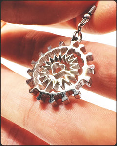 Close-up of a hand holding a 1-inch stainless steel dangly earring with Corona Heart design