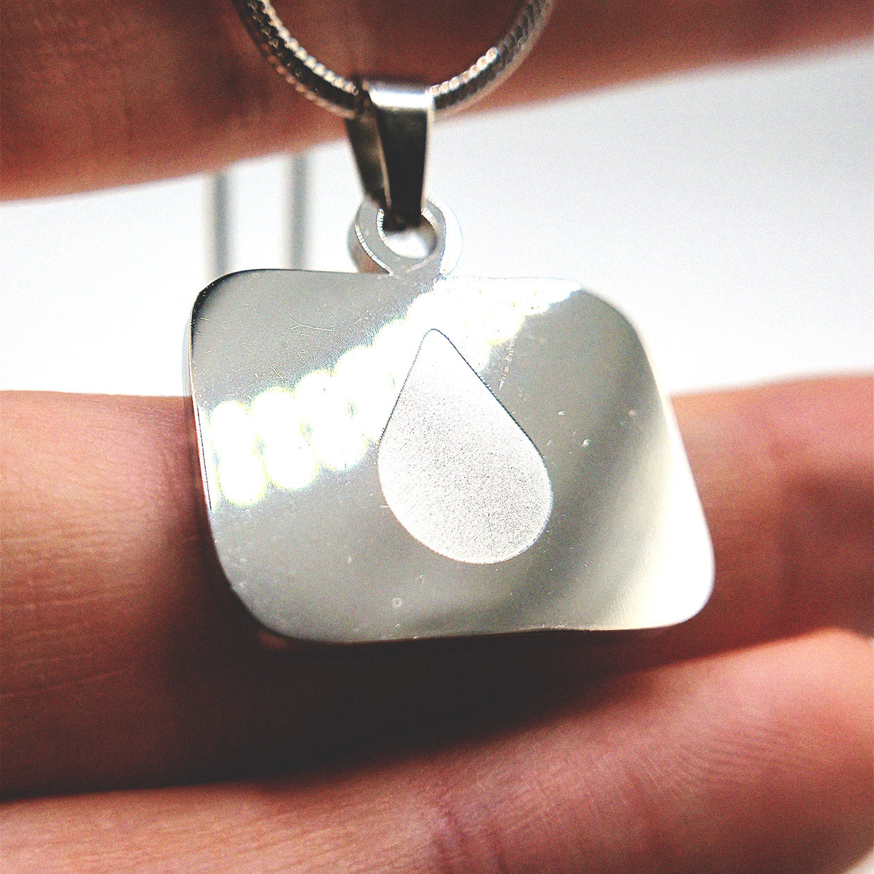 Lumon tear logo stainless steel necklace shown on a hand for size reference