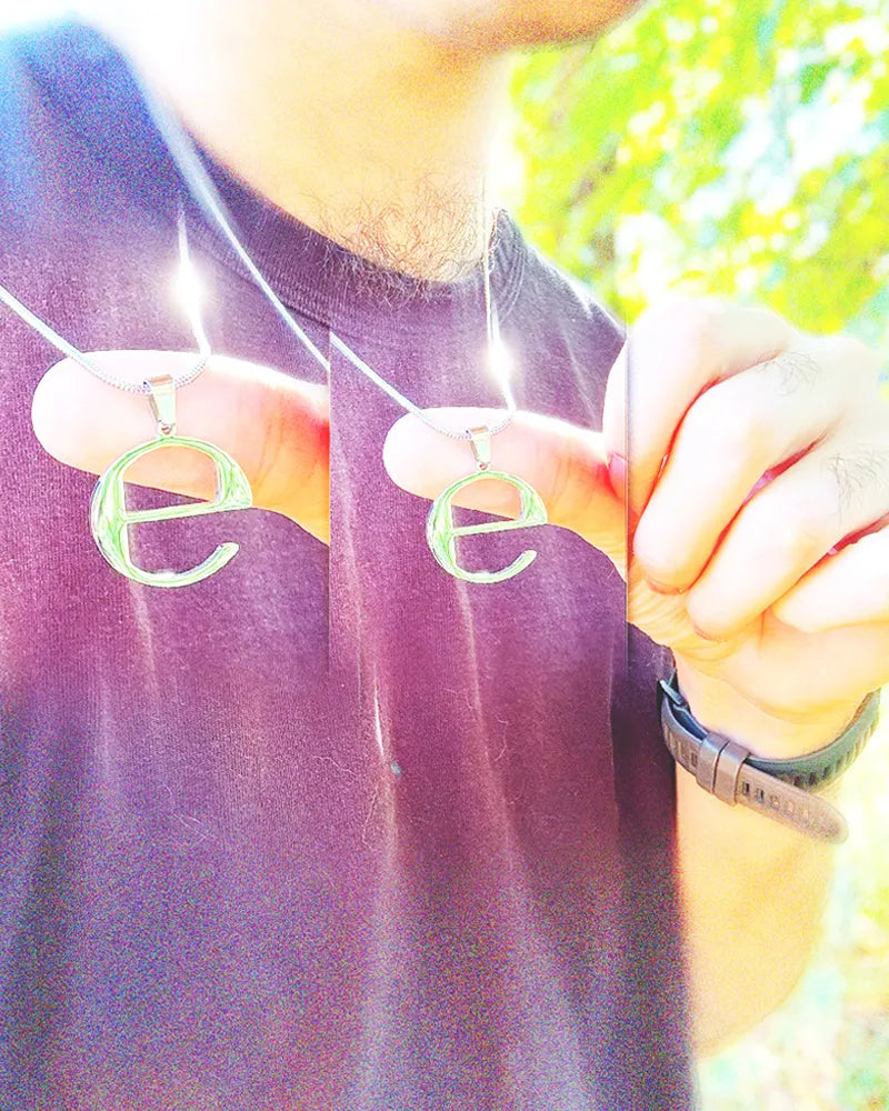 Image of man wearing and holding up a stainless steel shiny silver ecco2k "E" necklace chain, shining in sun