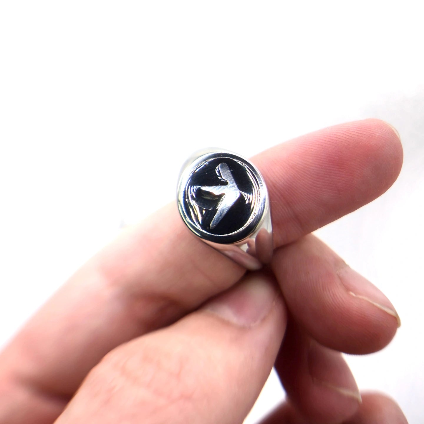 Finger holding a stainless steel silver ring with an Aphex Logo on a black circular base