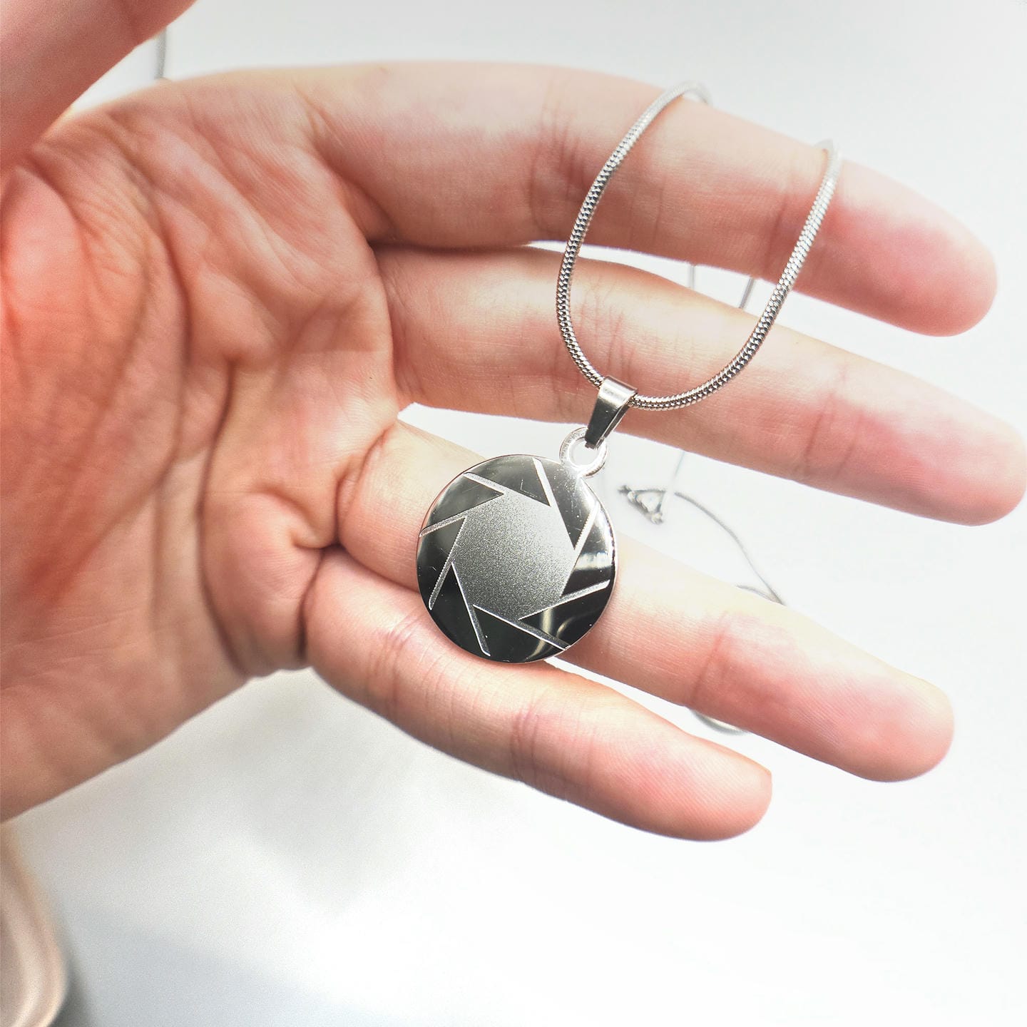 hand holding a stainless steel aperture science logo necklace from Portal 2