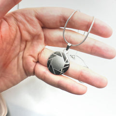 hand holding a stainless steel aperture science logo necklace from Portal 2