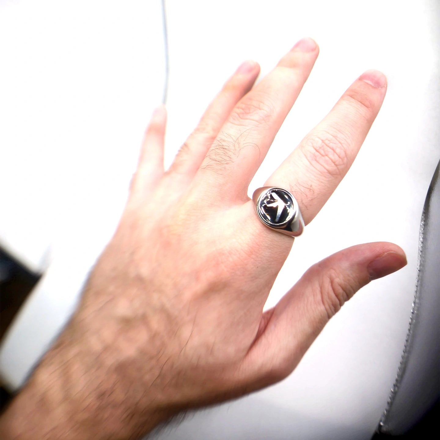 Hand wearing a silver aphex twin ring with a black stone on a white background